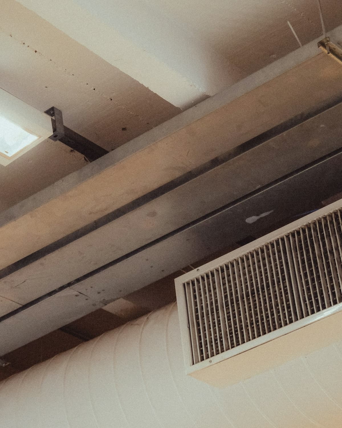 Insulated rectangular ductwork running along a ceiling beside a wall-mounted air grille
